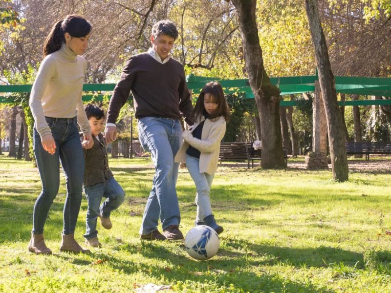 A family plays soccer together in a sunny park, enjoying quality time outdoors.